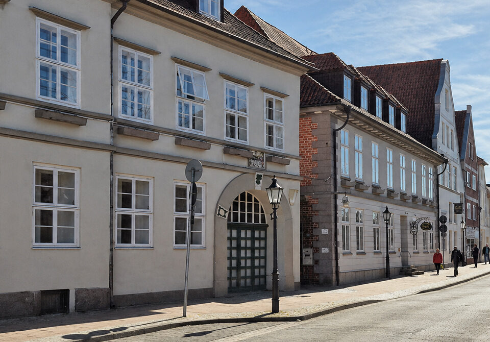 Historische Häuserzeile in der Neuen Sülze in Lüneburg mit klassizistischer Fassade und Rundbogenportal, Passanten auf Kopfsteinpflaster
